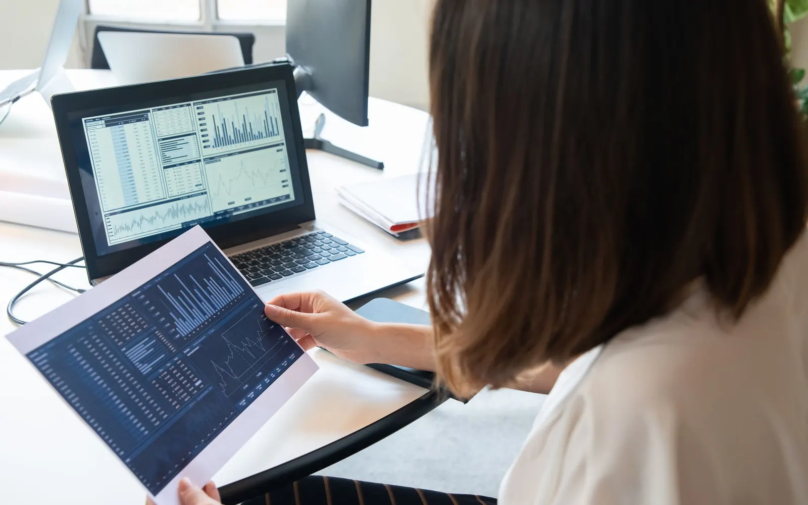 An analyst checking a printed chart against the numbers on her laptop