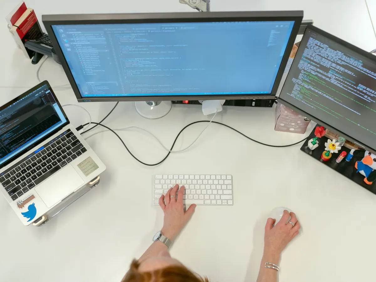 A data engineer at a desk with code on two monitors and a laptop