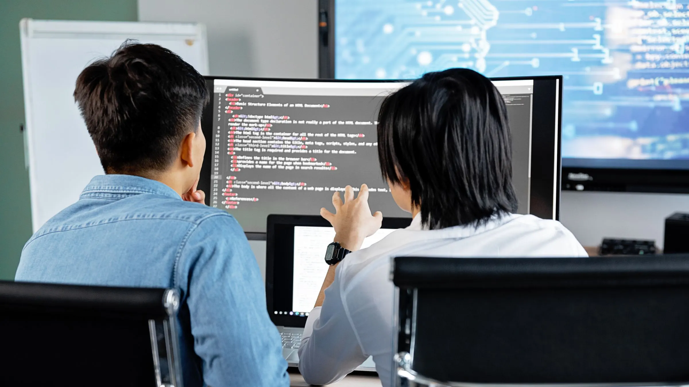 Two engineers review code together on large monitors