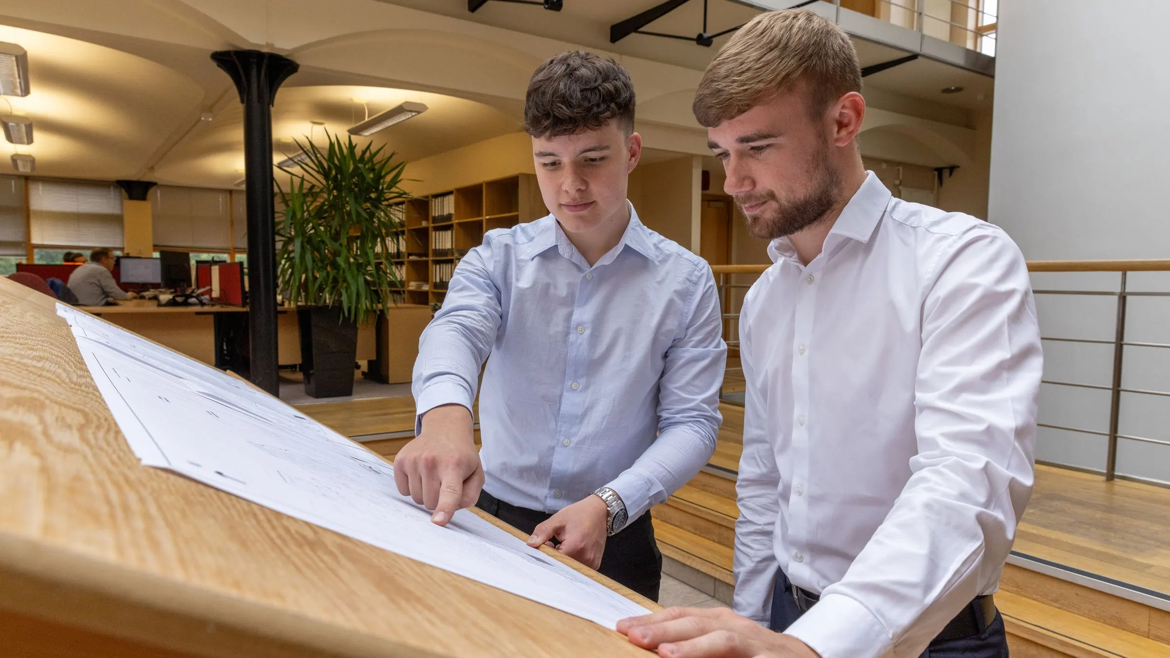 Two colleagues work through a plan together at a desk