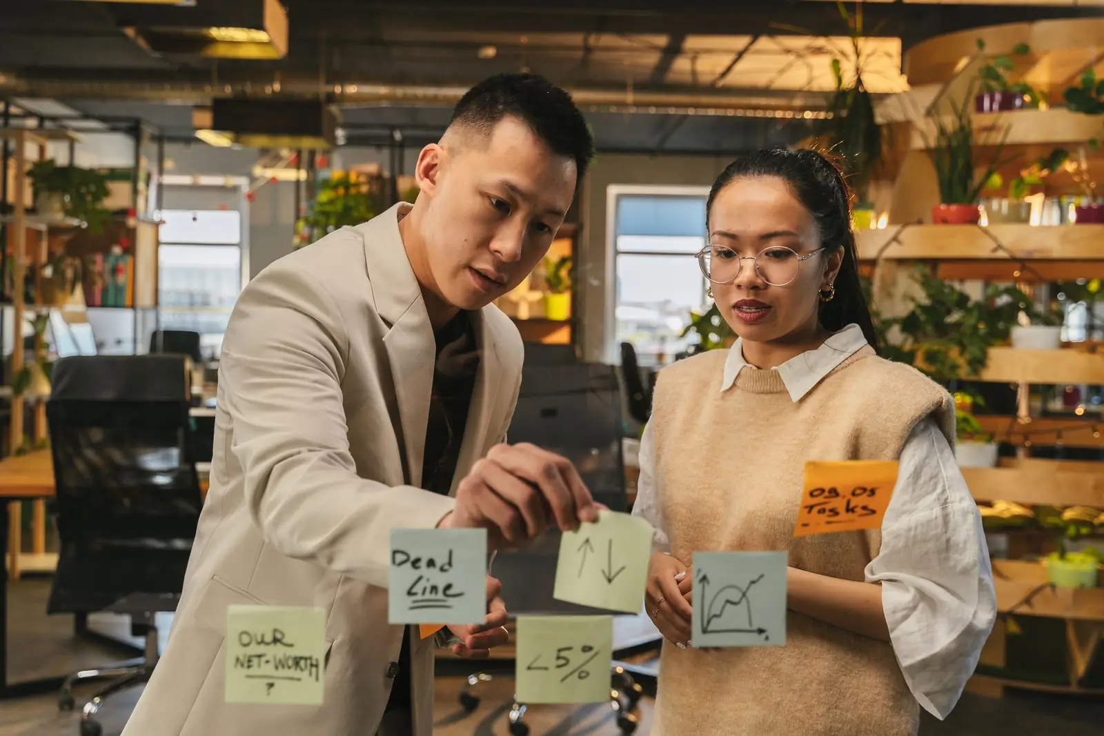 Two colleagues plan the work together on a glass wall covered in sticky notes